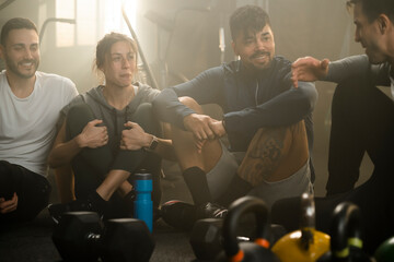 Sportsmen and a woman chatting together while sitting at the gym after exercising together. People resting and relaxing on the floor 