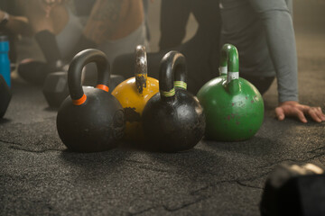 Obraz na płótnie Canvas Kettlebells kept on the gym floor after working out and friends sitting in the background