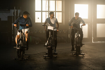 Fototapeta na wymiar A group of three young sportsmen exercising and riding stationary bike at gym
