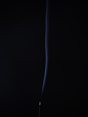 Obraz premium burning incense generating wisps of blue smoke on a black background