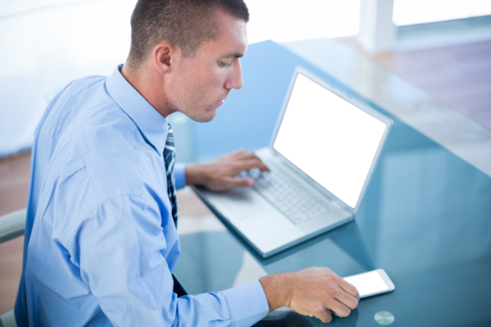 Businessman using mobile phone and laptop at desk