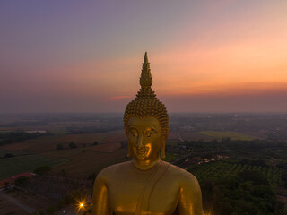 Obraz premium scenery sunset behind the great golden Buddha landmark of Thailand at wat Muang Ang Thong Thailand. .The largest Buddha statue in the world Surrounded by rice fields..colorful sky background. .