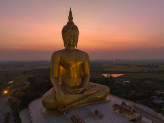 Obraz premium aerial view The moon was above the head of the biggest golden Buddha in the world..scenery red sky in twilight background. .golden big buddha is a popular landmark at wat Muang Ang Thong Thailand.