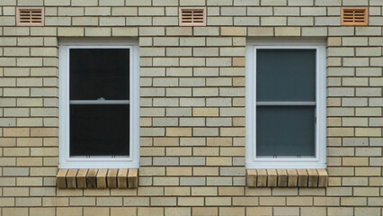 two windows with white timber frame against blonde brick wall with air vents