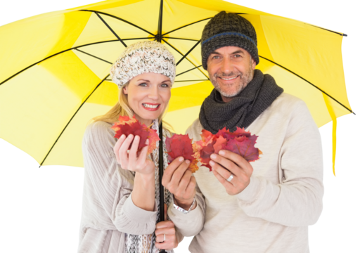 Portrait of couple holding autumn leaves while standing under yellow umbrella