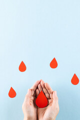 Fototapeta premium Hands of caucasian woman cupping blood drop, with blood drops on blue background, copy space
