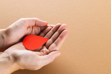 Hands of caucasian woman cupping blood drop on brown background with copy space
