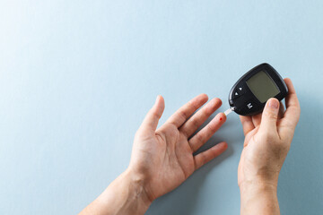 Fototapeta premium Hands of caucasian woman taking blood sugar reading with glucometer, on blue background