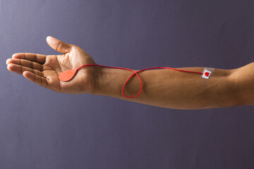 Arm of biracial man with heart sticking plaster and red string with blood drop, on grey background