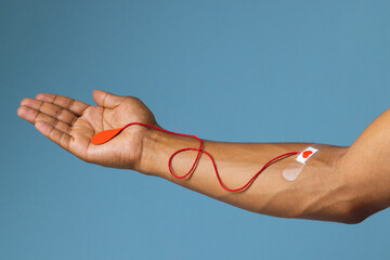 Arm of biracial man with heart sticking plaster and red string with blood drop, on blue background