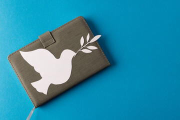 Close up of white dove with leaf over notebook and copy space on blue background