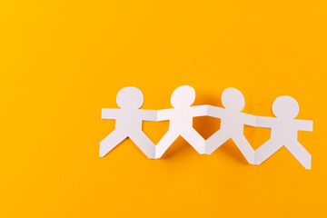Close up of four paper cut out people figures holding hands with copy space on yellow background