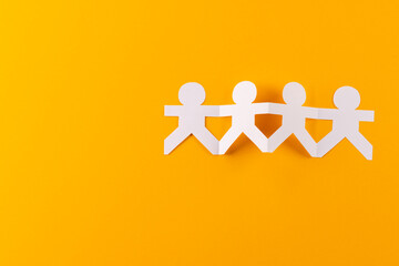 Close up of four paper cut out people figures holding hands with copy space on orange background