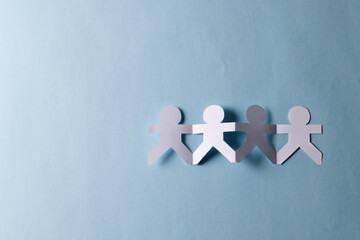 Close up of four paper cut out people figures holding hands with copy space on blue background