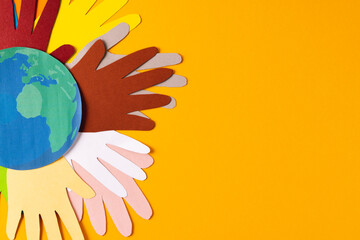 Fototapeta na wymiar Paper cut out of multi coloured hands and globe with copy space on yellow background
