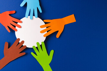 Paper cut out of multi coloured hands and white circle with copy space on blue background