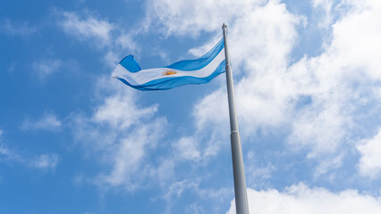 The flag of Argentina against the sky and clouds. A blue-and-white banner with the image of the sun...