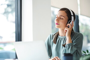 Relaxed young businesswoman in headphones enjoying music podcast using laptop app, smiling female millennial student or office worker wearing headset listening to new favorite audio tracks. 