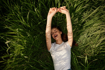 happy woman lies in high grass lit by the sun stretching her hands to the camera