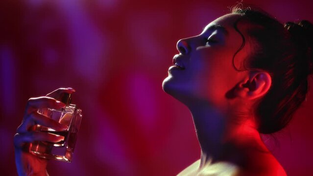 Fashion brunette woman spraying perfume bottle fragrance aroma sensual cosmetic at dark shadow neon