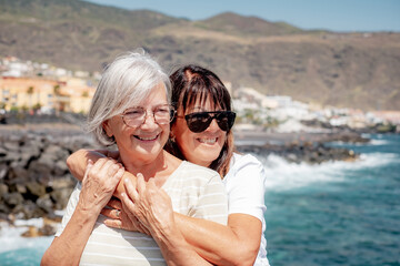 Portrait of Happy Caucasian Senior Couple of Women Hugging in Vacation at Sea Standing Under the...