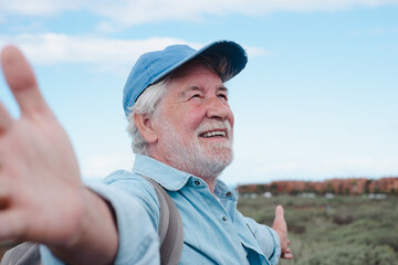 Happy senior man with hat with open arms in a trekking day in country footpath, enjoying healthy lifestyle and freedom, vacation or retirement concept