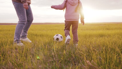 little child with his father plays soccer ball field sunset. childhood dream playing football....