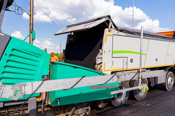 Truck is loading hot asphalt into spreader, tarmac road laying spreader machine