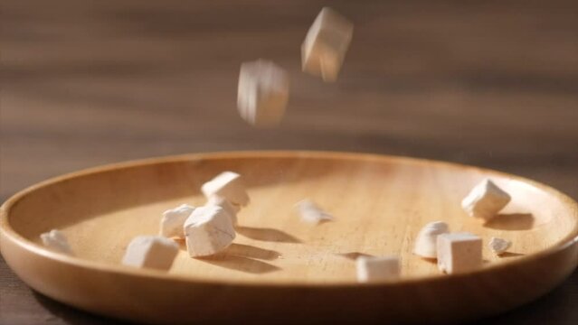 Close view of wolfiporia extensa falling on round wooden plate on dark table. Slow motion scene with traditional medicine, wolfiporia extensa has effects: anti-oxidant, anti-cancer, anti-viral
