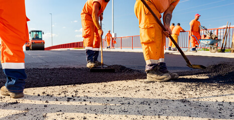 Workers are using shovels for realign hot asphalt to correct measure
