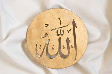 Allah bismillah names close up. Golden wooden calligraphy of islamic god. on white textile, top...