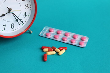 On a turquoise background are medicines and an alarm clock.