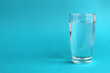 A transparent glass of water stands on a turquoise background.
