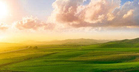 countryside sunset in green hills of spring fields with old castle farm and mountains on background of evening landscape