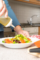 Close up of woman putting olive oil on a fresh salad of tomatoes, lettuce and carrots in the kitchen at home. Healthy and easy to make food concept. High quality photo