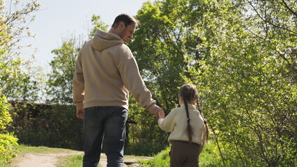 father child walk through woods holding hands. happy family. hand hand. dad with kid daughter girl...