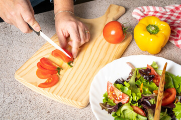 Female hand cut tomatoes on rustic kitchen table, around lie ingredients and vegetables. Healthy foods, cooking and vegetarian concept. High quality photo