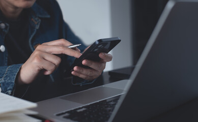 Asian business woman sitting at table using mobile phone, online working on laptop, searching the information on internet network. Online education, e-learning concept