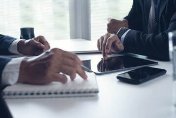 Two businessmen sitting at table, using digital tablet and laptop co-working at modern office,...