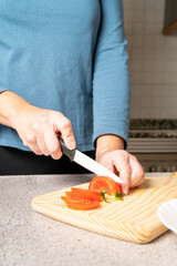 Unrecognizable woman cuts tomatoes on a wooden board in the kitchen at home. Healthy food preparation concept. High quality photo