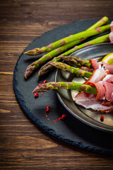 Uncooked green asparagus with prosciutto on wooden table
