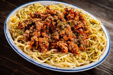 Spaghetti with minced meat, tomato sauce, parmesan cheese and seasonings served on wooden table
