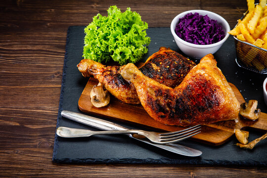 Barbecue chicken thighs with french fries, lettuce and red cabbage salad on wooden table
