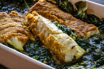 Fish dish - roast cod fillet with potatoes and spinach served on stone plate on wooden table
