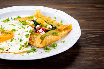 Savory crepes with feta, fried vegetables and egg on wooden background