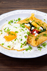 Savory crepes with feta, fried vegetables and egg on wooden background