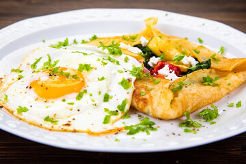 Savory crepes with feta, fried vegetables and egg on wooden background
