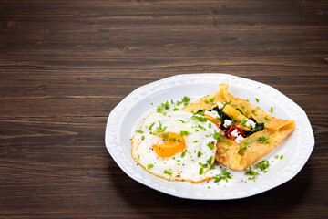 Savory crepes with feta, fried vegetables and egg on wooden background