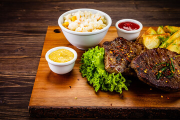 Fried beef sirloin with potatoes and vegetables on wooden table