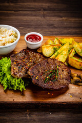 Fried beef sirloin with potatoes and vegetables on wooden table
